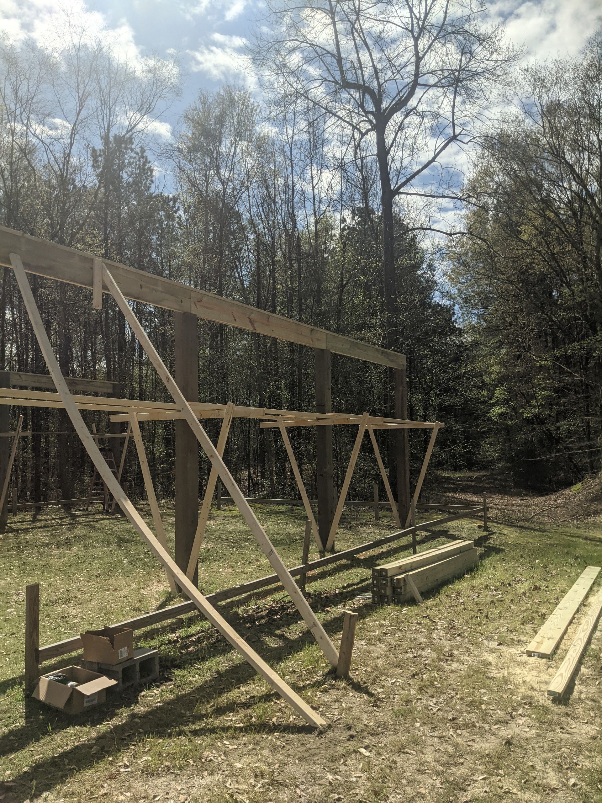 Wooden support beams and scaffolding structures for a construction project set in a wooded area on a sunny day.