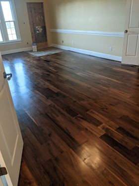 Empty room with dark hardwood floors, beige walls, and a window letting in sunlight.