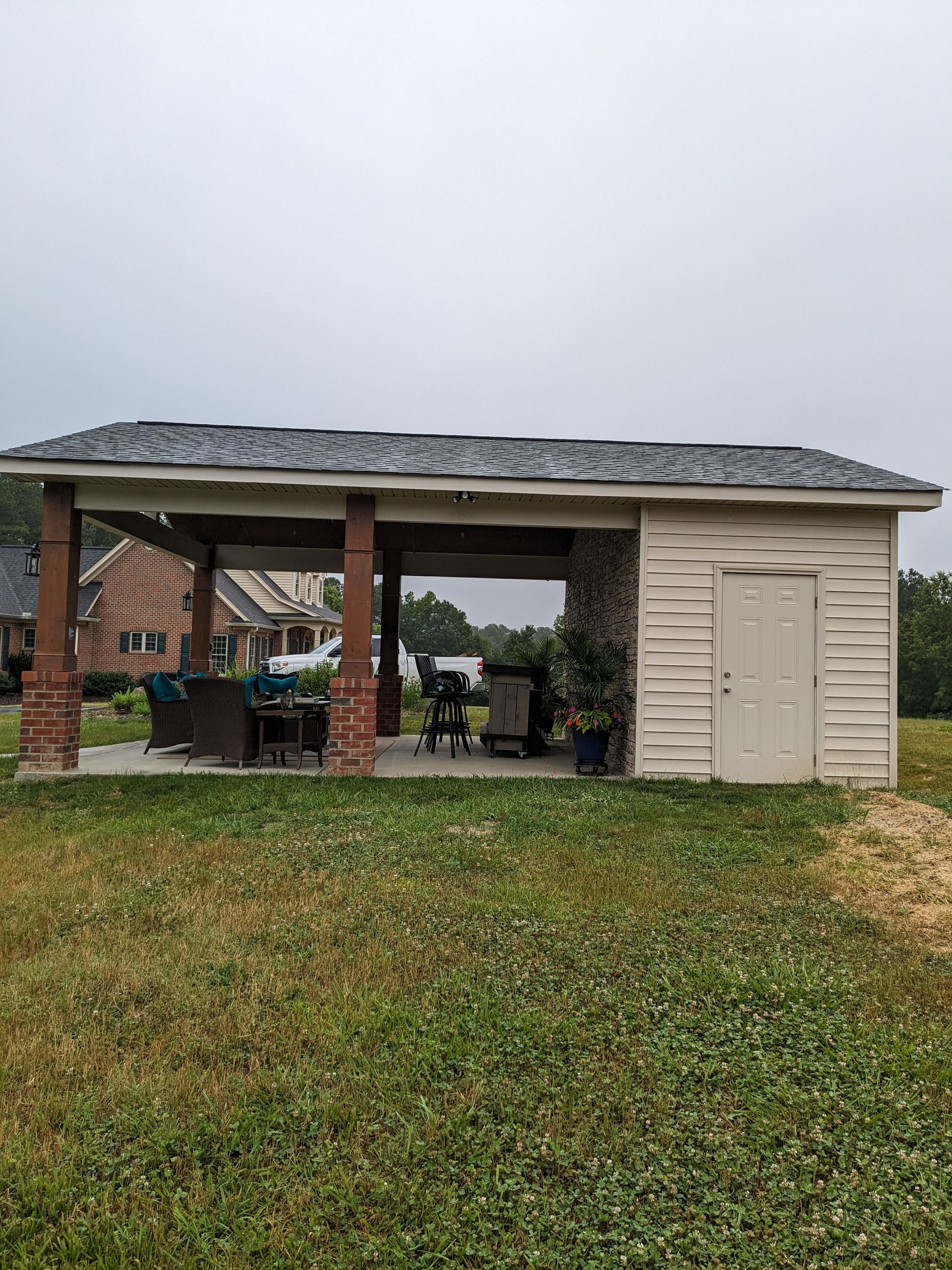 A backyard structure featuring an open-air covered patio with stone-based pillars next to a small, enclosed storage room.