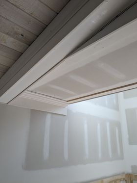 White interior ceiling corner with exposed beams and a partially open window shade casting shadows on the wall