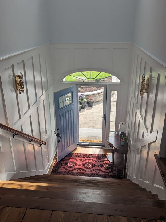 Stairway descending to an open front door with daylight, blue door, and red rug at the entry.