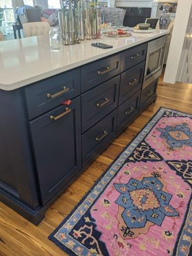 Navy kitchen island with white countertop beside a colorful patterned rug on hardwood floor.