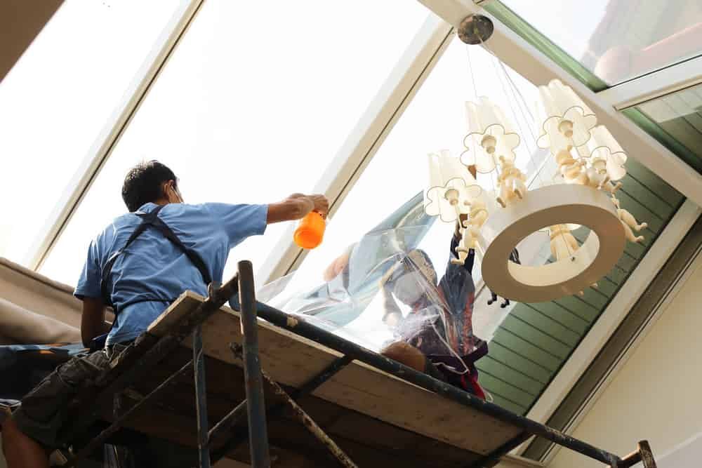a Man is Cleaning a Window While Sitting on a Scaffolding — Total Tint Bendigo in East Bendigo, VIC