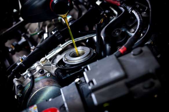 Pouring oil into a car engine during an oil change; yellow oil, dark engine parts.