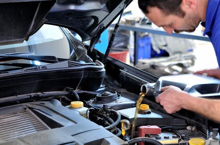 Mechanic pouring oil into a car engine with the hood open.
