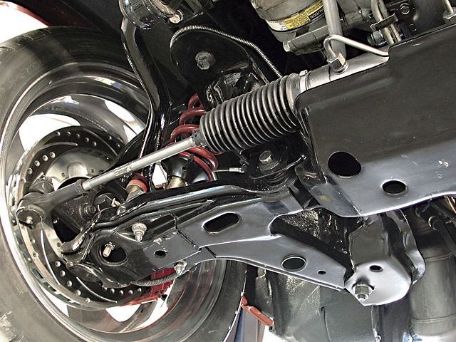 Black car suspension with steering rack, wheel, and red coil spring.