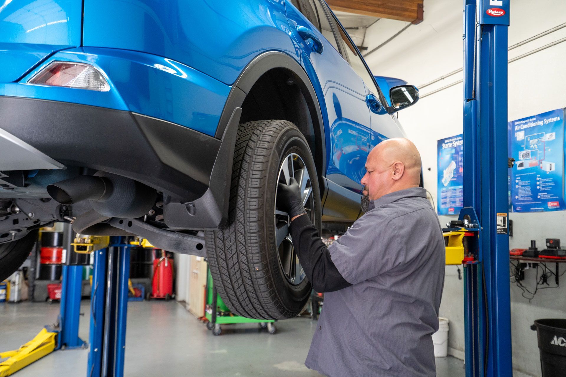 Mechanic working on the raised wheel of a blue SUV in a garage.