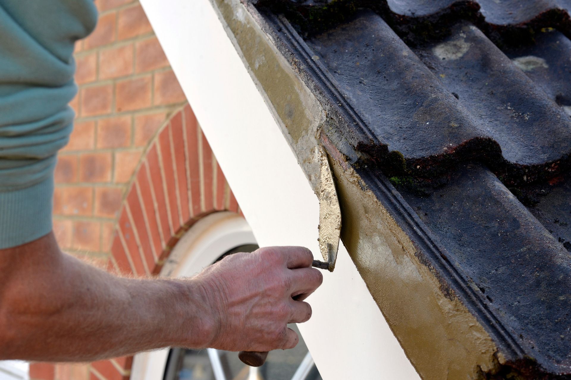A masonry service contractor applying cement for roof edge tiling.
