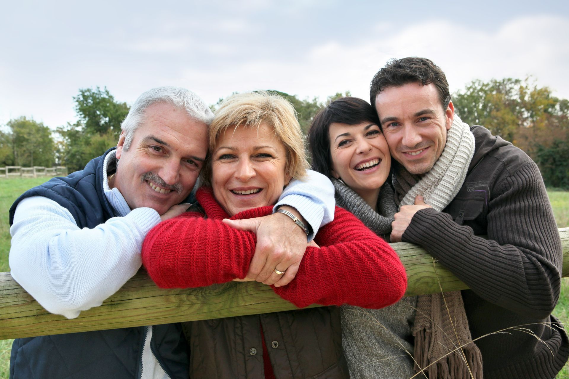 A family is posing for a picture while leaning on a wooden fence.