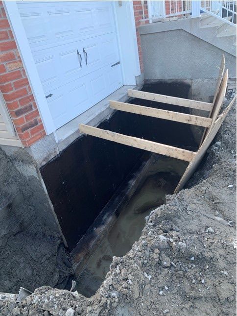 Puits de lumière ouvert au sous-sol avec des planches de bois à côté des fondations de la maison