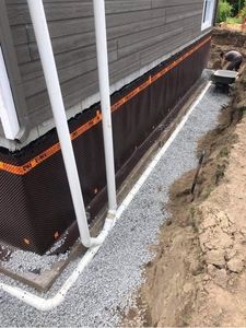 Étanchéité des fondations avec membrane de drainage noire et gravier le long d'un mur de maison et de canalisations