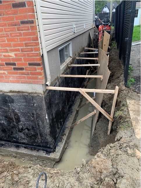 Tranchée étroite à côté d'une maison en briques avec des étais en bois et de l'eau boueuse en construction