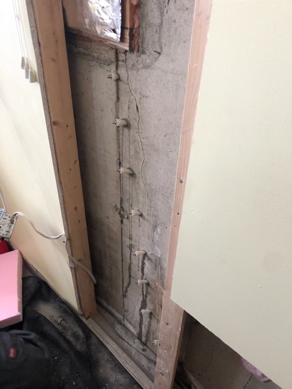 Cavité murale endommagée avec bois et isolant apparents à côté d'une armoire blanche dans une pièce