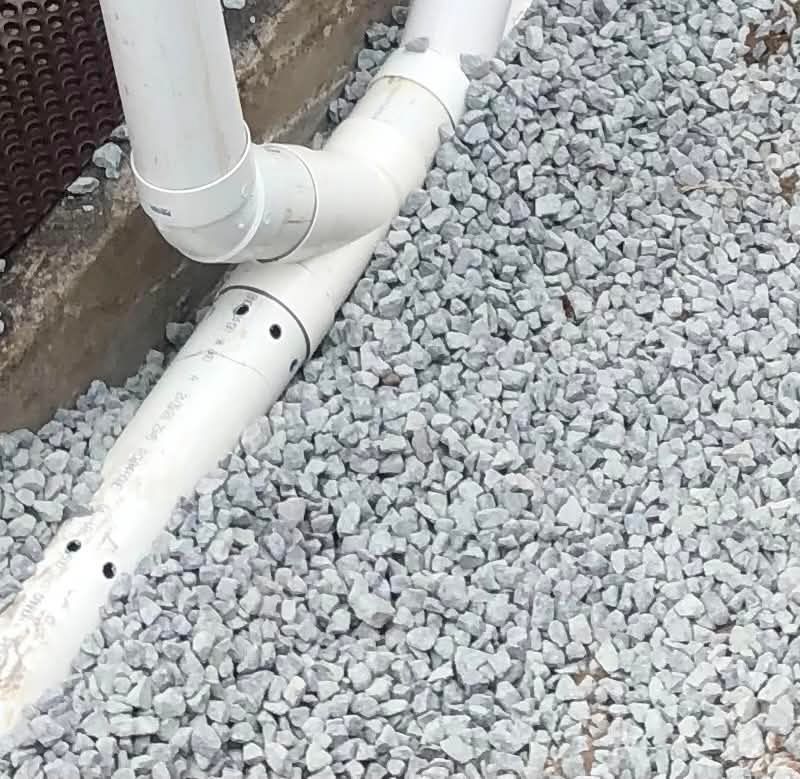 Tuyaux de drainage en PVC blanc sur du gravier gris le long d'un mur
