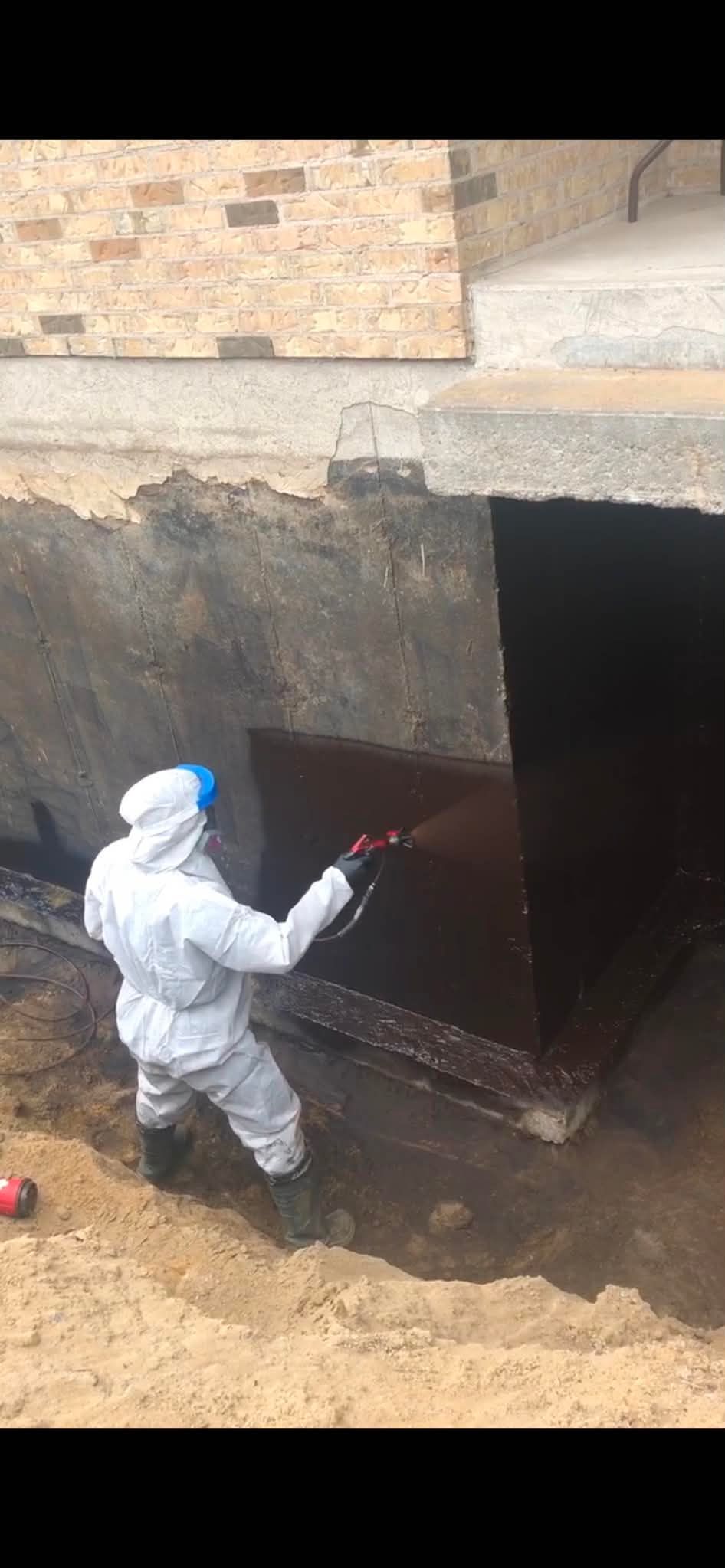 Personne en combinaison de protection peignant au rouleau une structure souterraine en béton sombre.