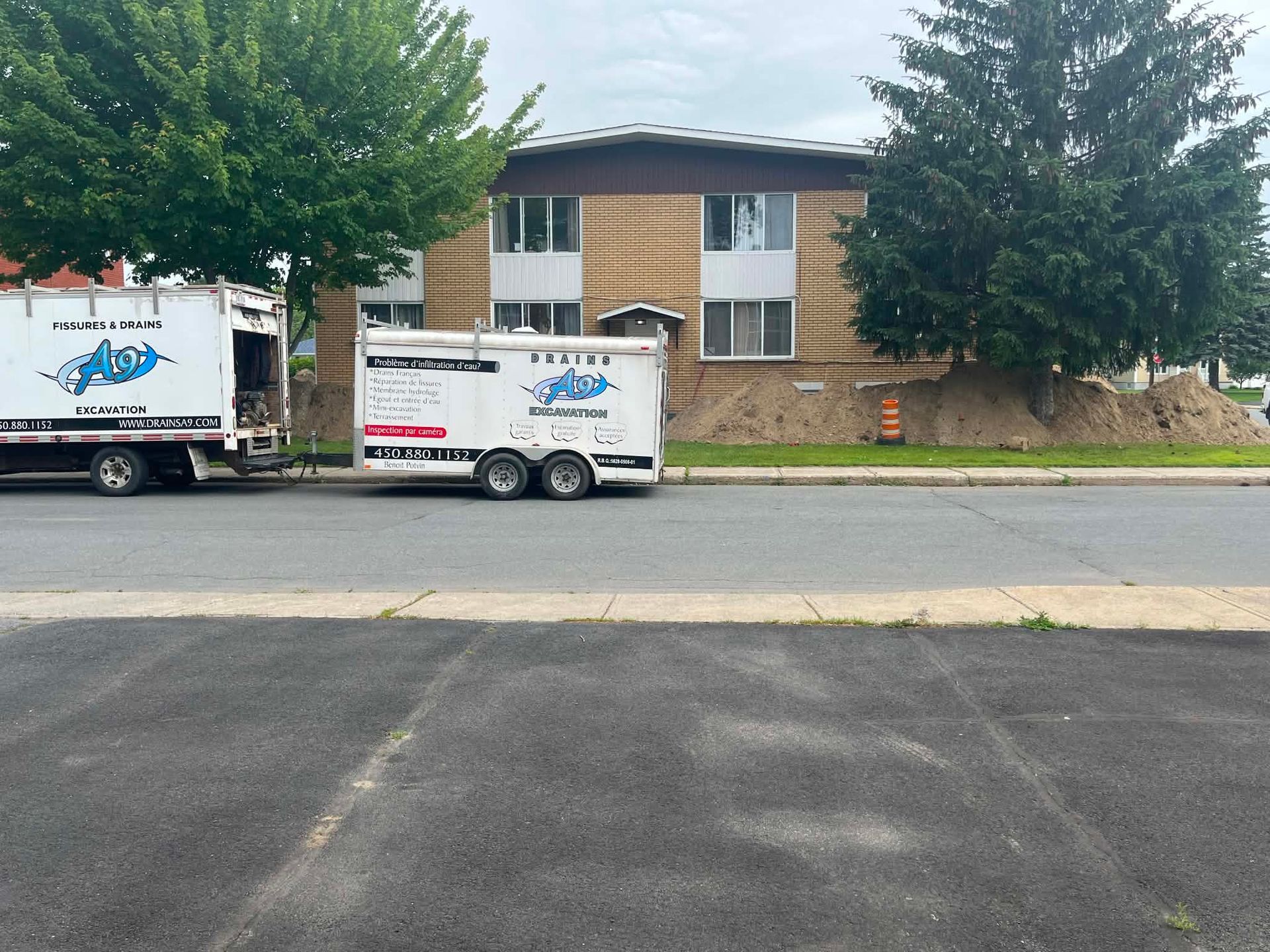 Deux camions de déménagement blancs stationnés dans la rue, devant une maison en briques et des arbres
