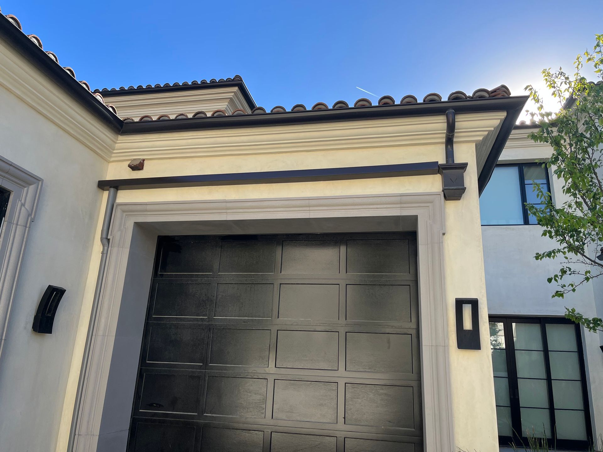 Garage with dark door, cream-colored walls, and dark trim. Sunny day.