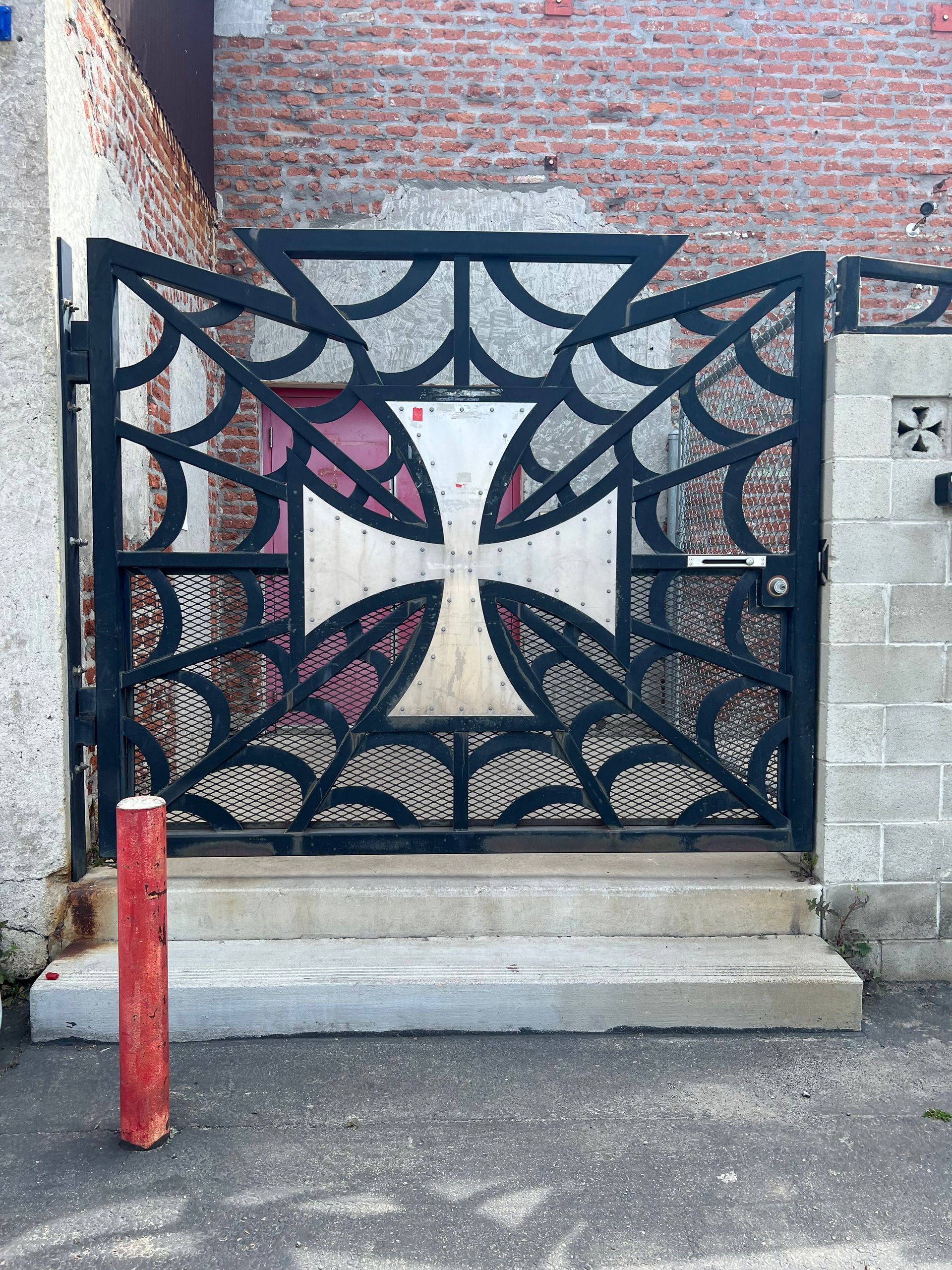 Black metal gate with a white cross, brick background.