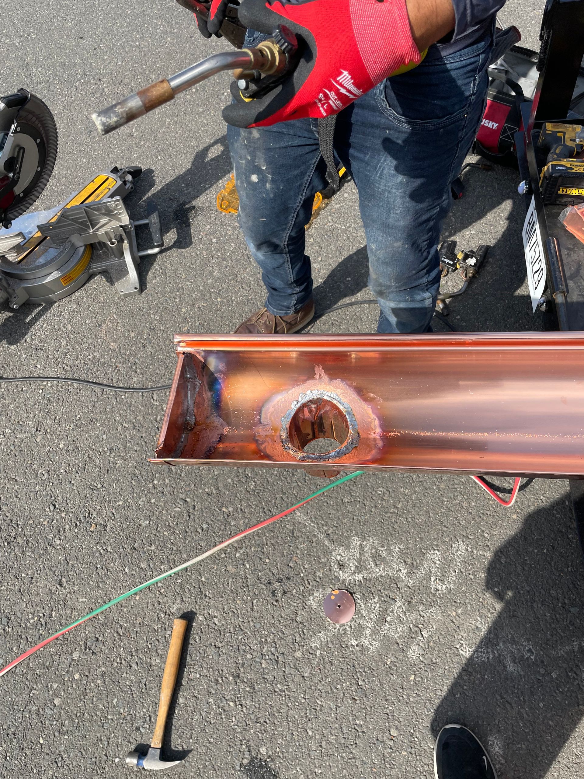 Person welding copper gutter, wearing red gloves and jeans, outdoors.