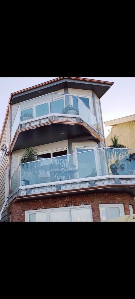 Multi-story house with glass balconies, brick facade, and tile roof.