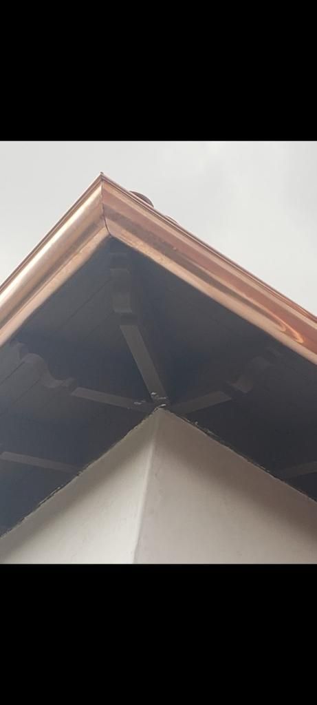 A copper-trimmed roof corner with a dark underside and a white wall below, suggesting a building exterior.