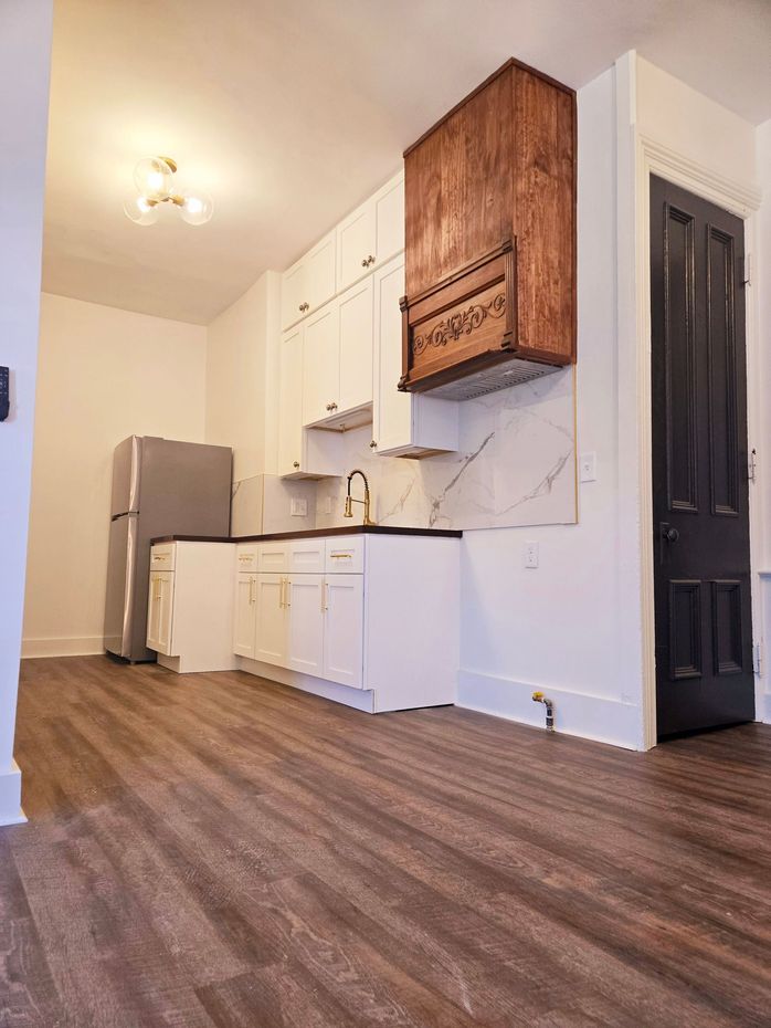 Beautiful kitchen in renovated apartment with white cabinets running up to the ceiling and a custom wood hood vent.