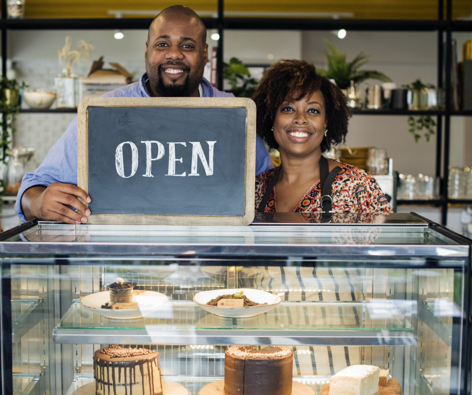 A man and a woman are standing in front of a display case holding a sign that says `` open ''.