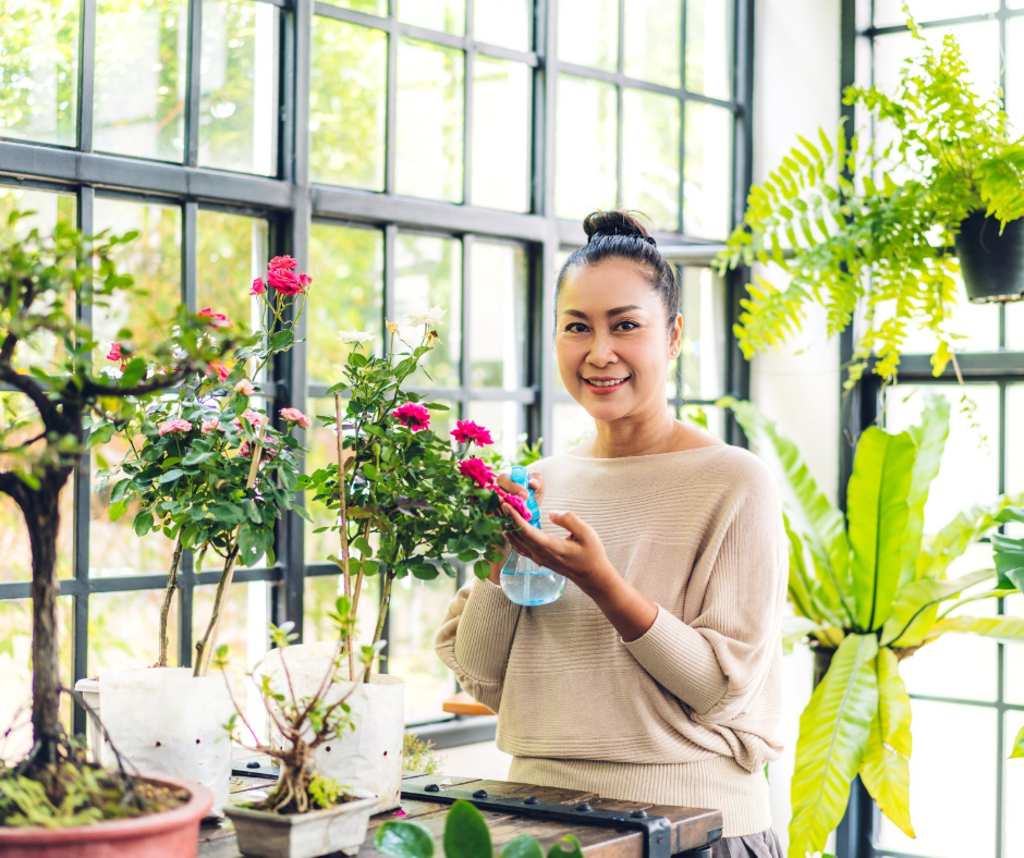 A woman is watering a bonsai tree in a greenhouse.