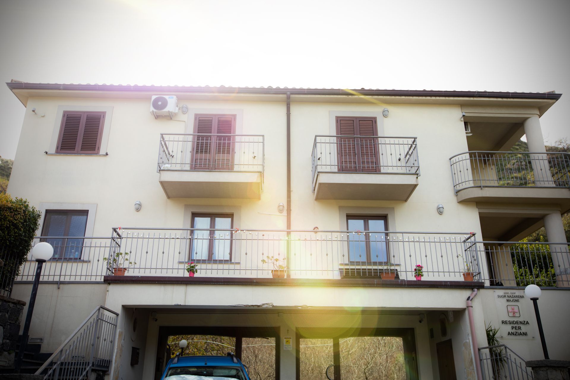 Edificio color crema a due piani con balconi. Le finestre hanno persiane marroni. Un'auto è parcheggiata sotto.