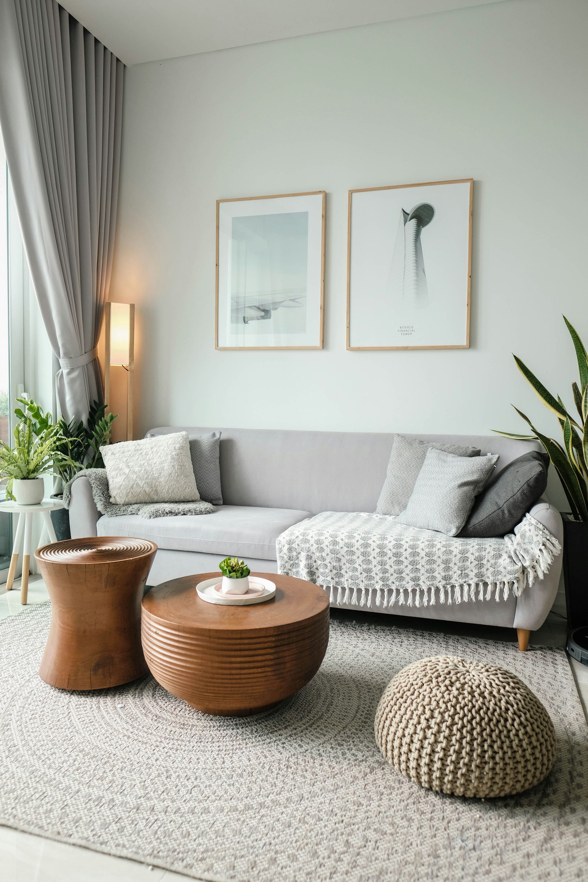Cozy living room with a gray sofa, woven coffee tables, wall art, and textured pouf by a window
