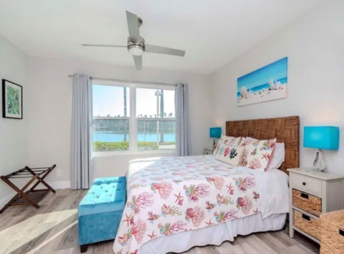 Bright bedroom with a large bed, blue headboard, wood nightstands, and a window with a scenic view.