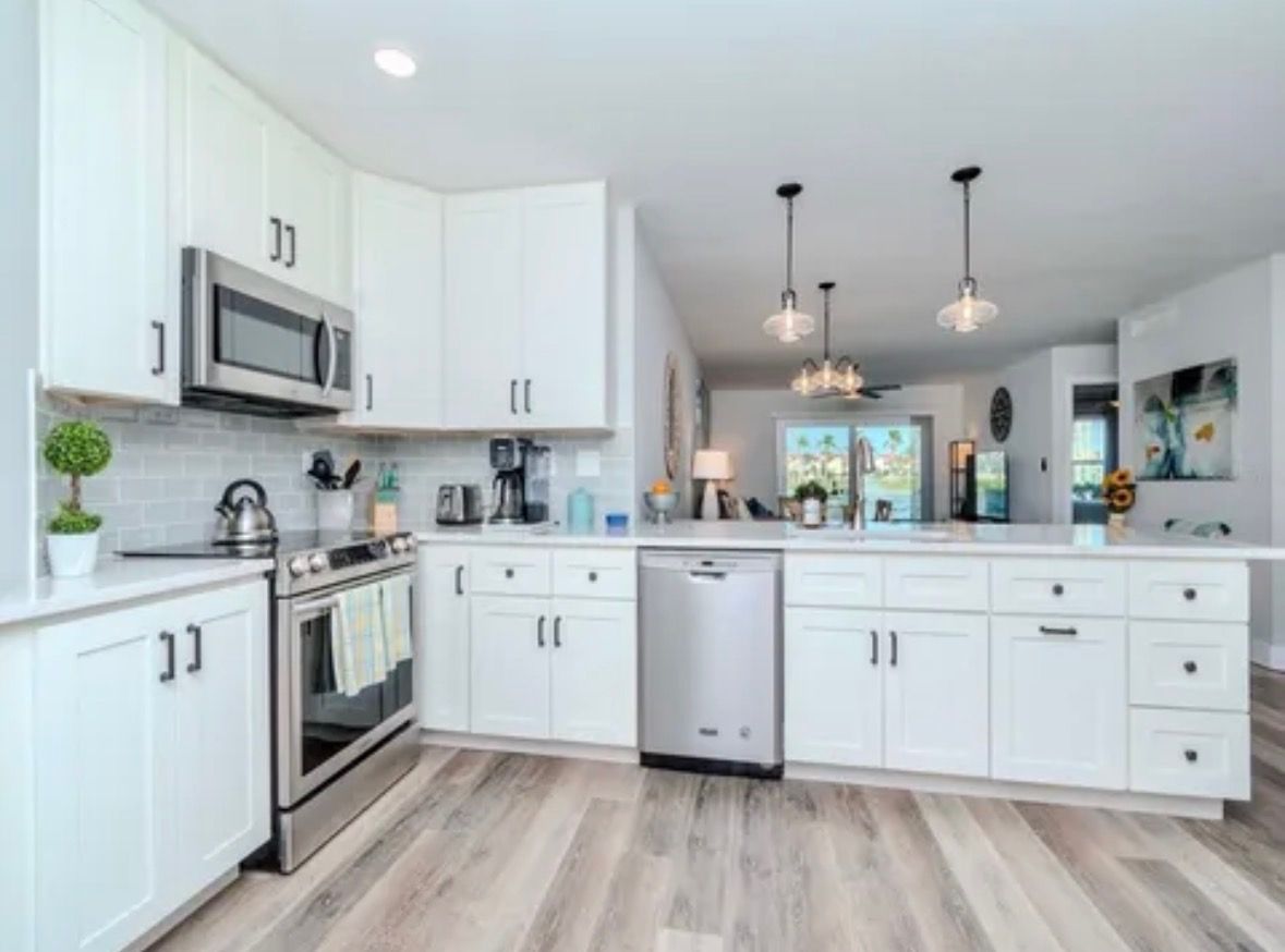 Bright modern white kitchen with stainless appliances, island, and gray wood flooring