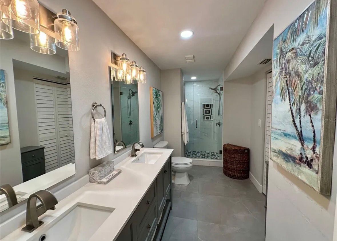Bright modern bathroom with long double vanity, mirrors, shower, and beach artwork on the wall.