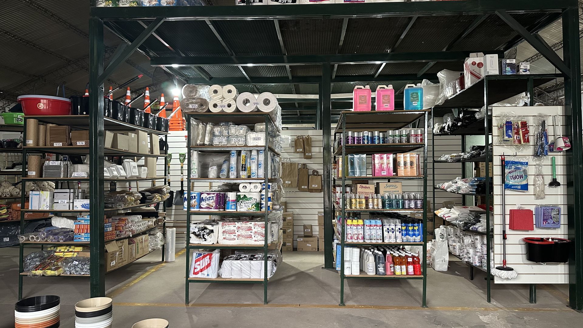 Pasillo interior de tienda con estantes metálicos repletos de productos variados y botellas coloridas.