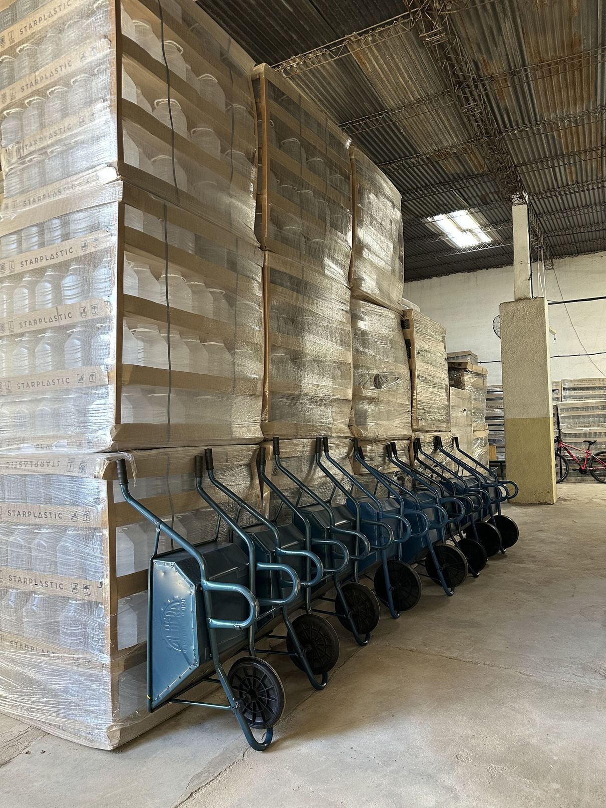 Carretillas apiladas en fila en un almacén junto a palés altos envueltos.