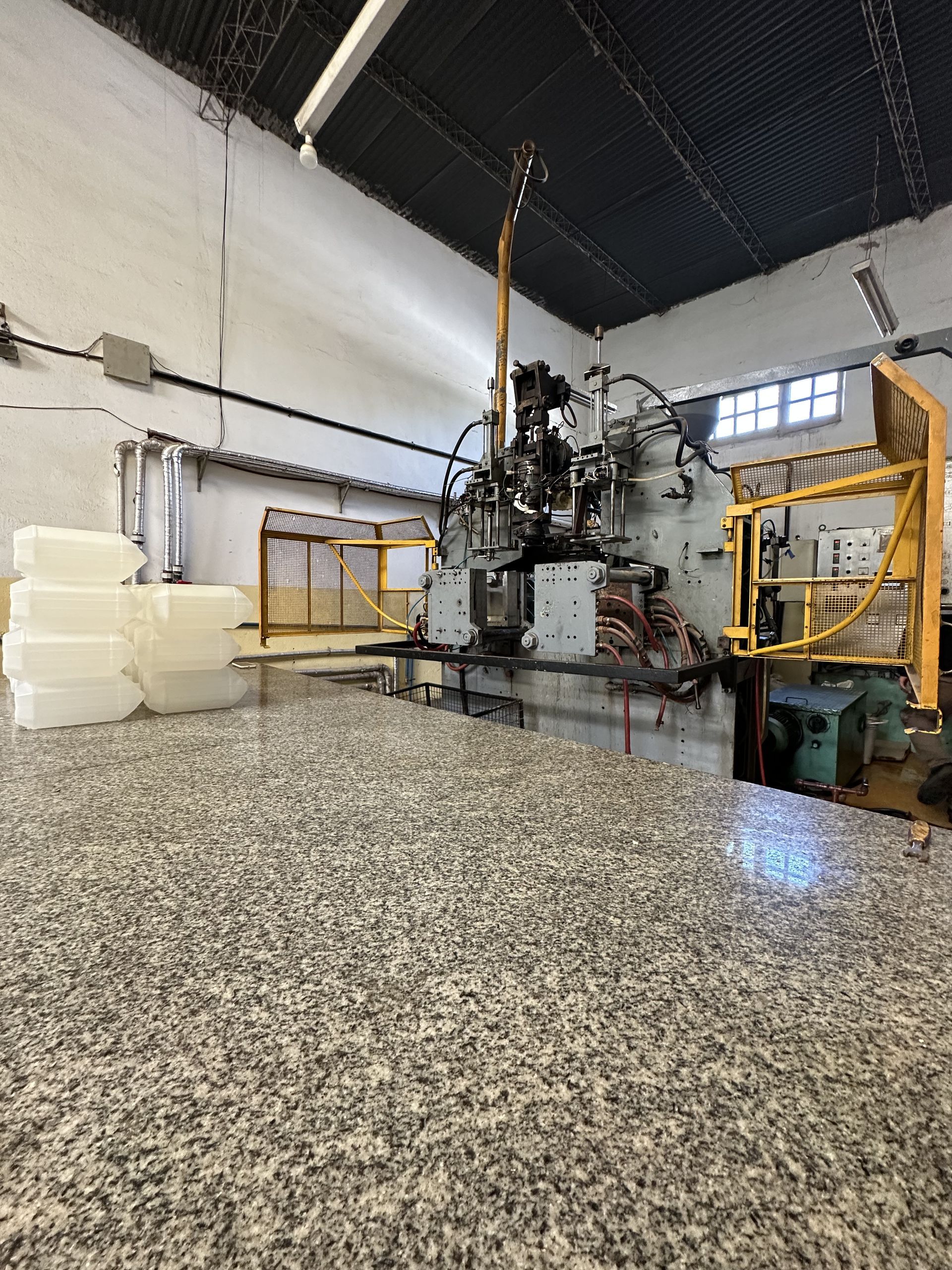 Planta de una fábrica industrial con una gran máquina, bloques de espuma blanca apilados y un suelo de hormigón moteado.