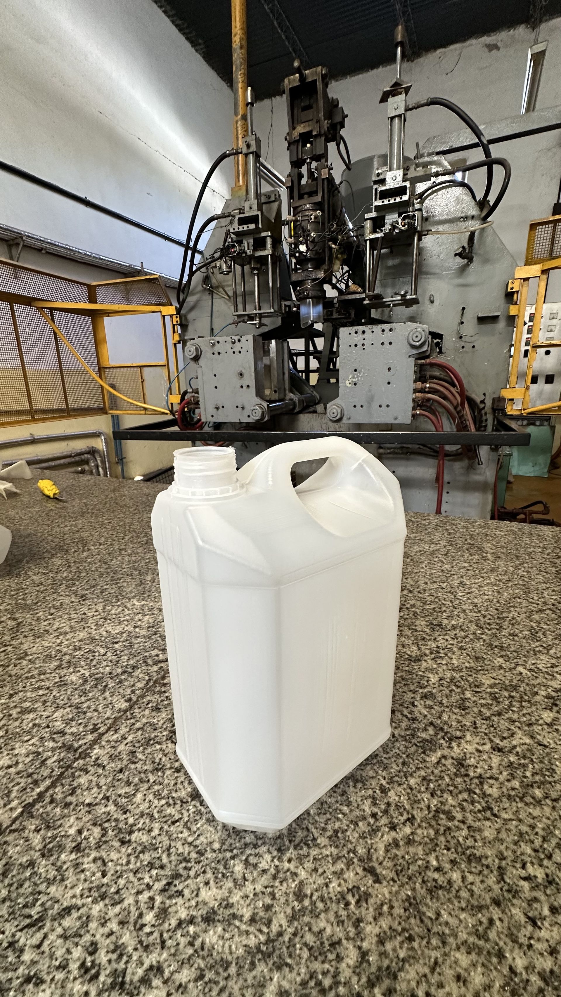 Bidón de plástico blanco sobre una encimera en un taller industrial con maquinaria al fondo.