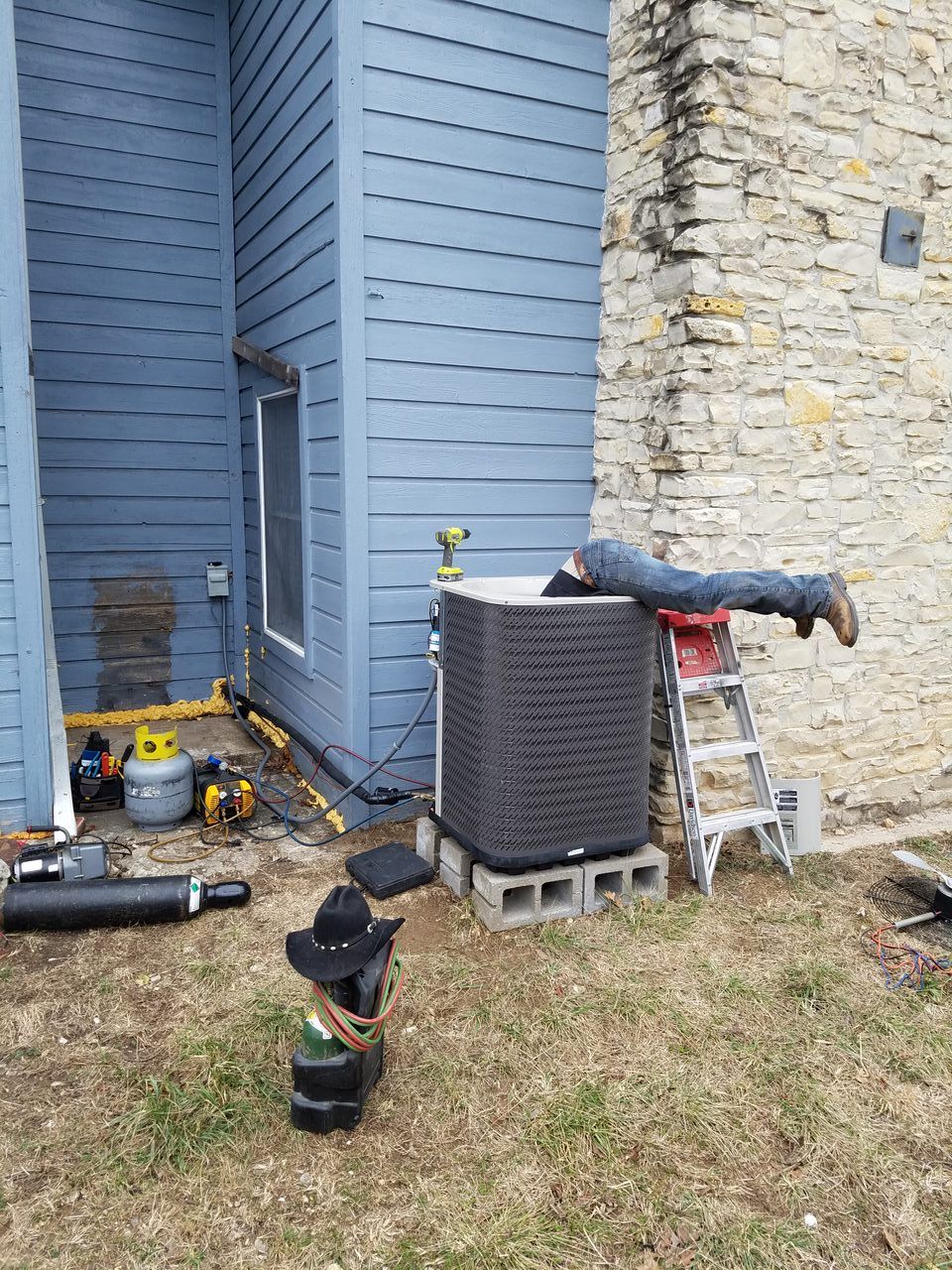 A man is laying on the ground next to an air conditioner.