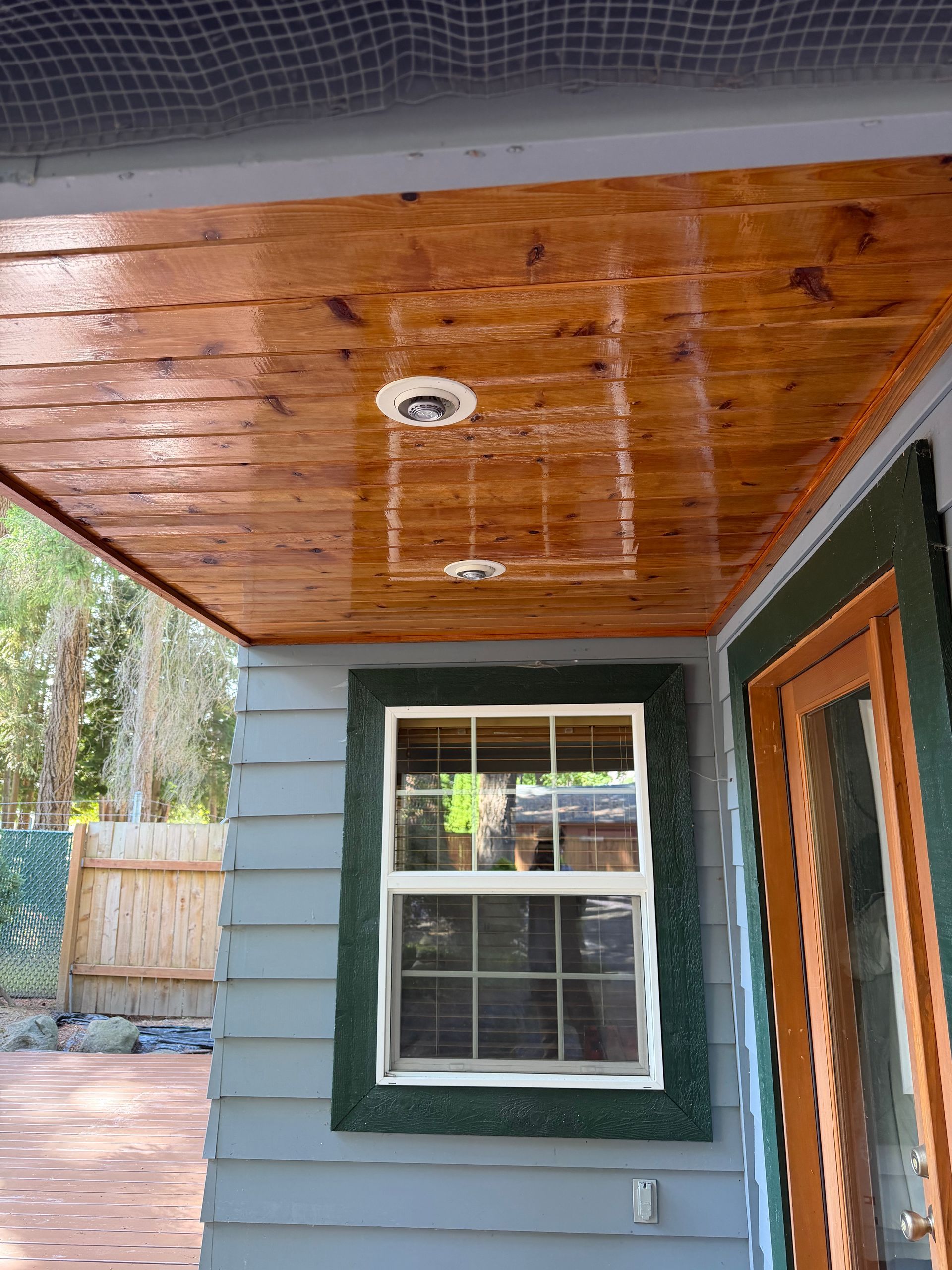 Covered porch ceiling with wood paneling, recessed light, and a window beside a green-trimmed door
