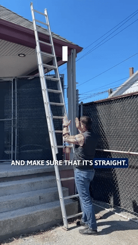 Person holding a ladder against a house exterior under a blue sky