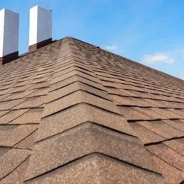 Brown shingle roof with two white chimneys against a blue sky.