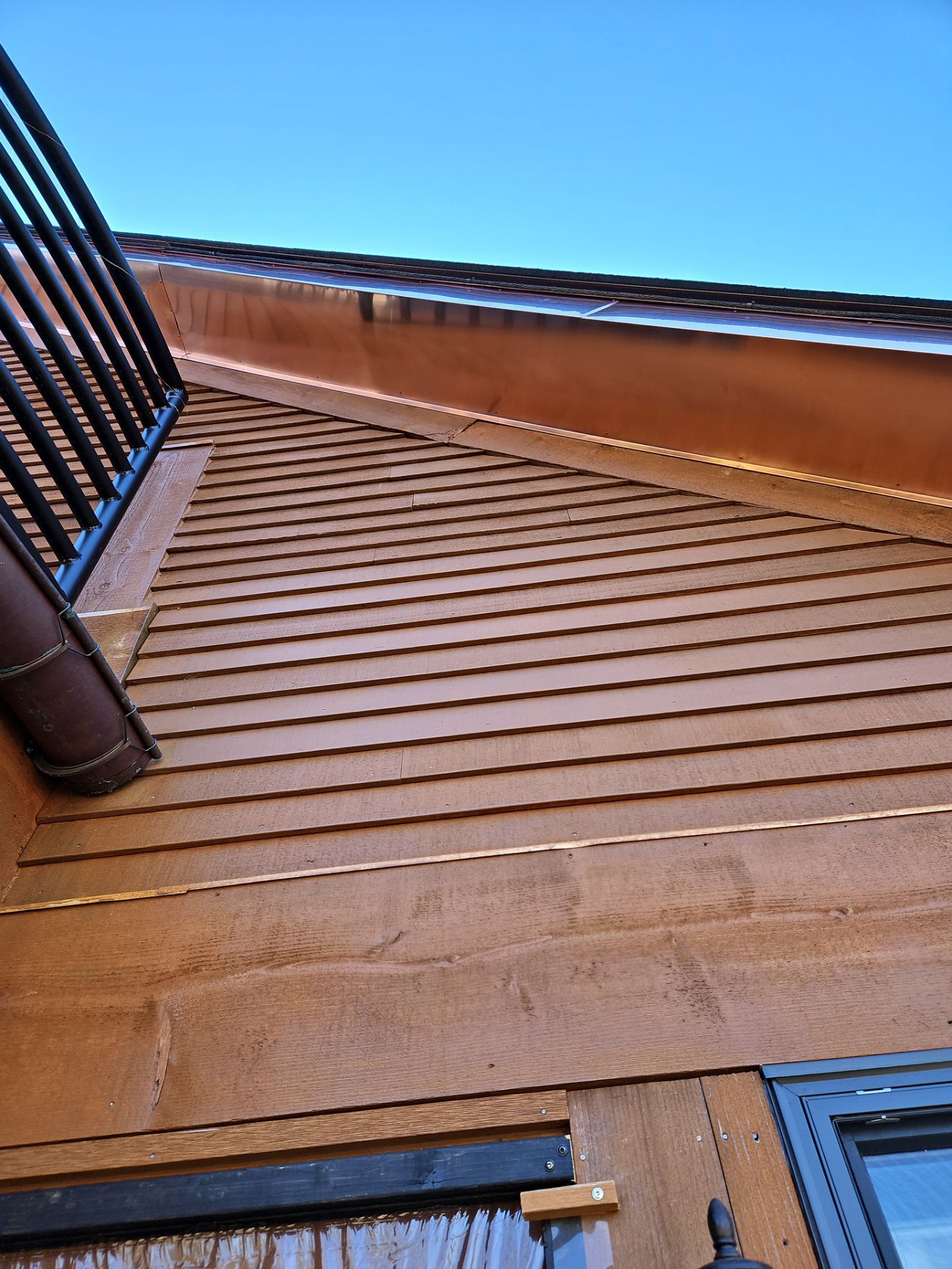 Brown wooden exterior of a building with a section of black railing and a clear blue sky.