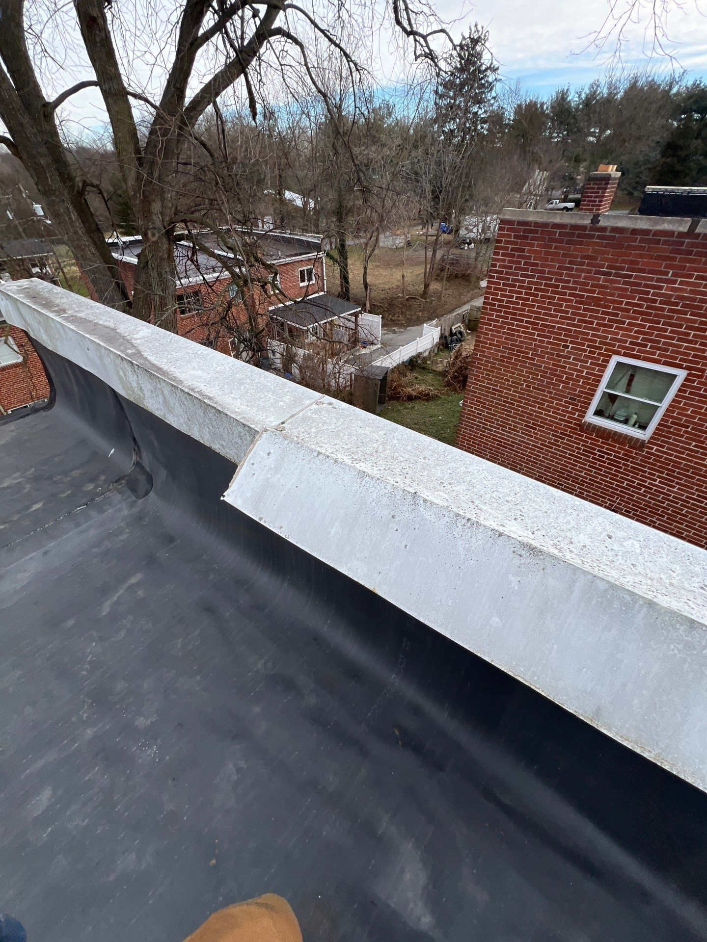 Black flat roof with silver edging, overlooking residential neighborhood.