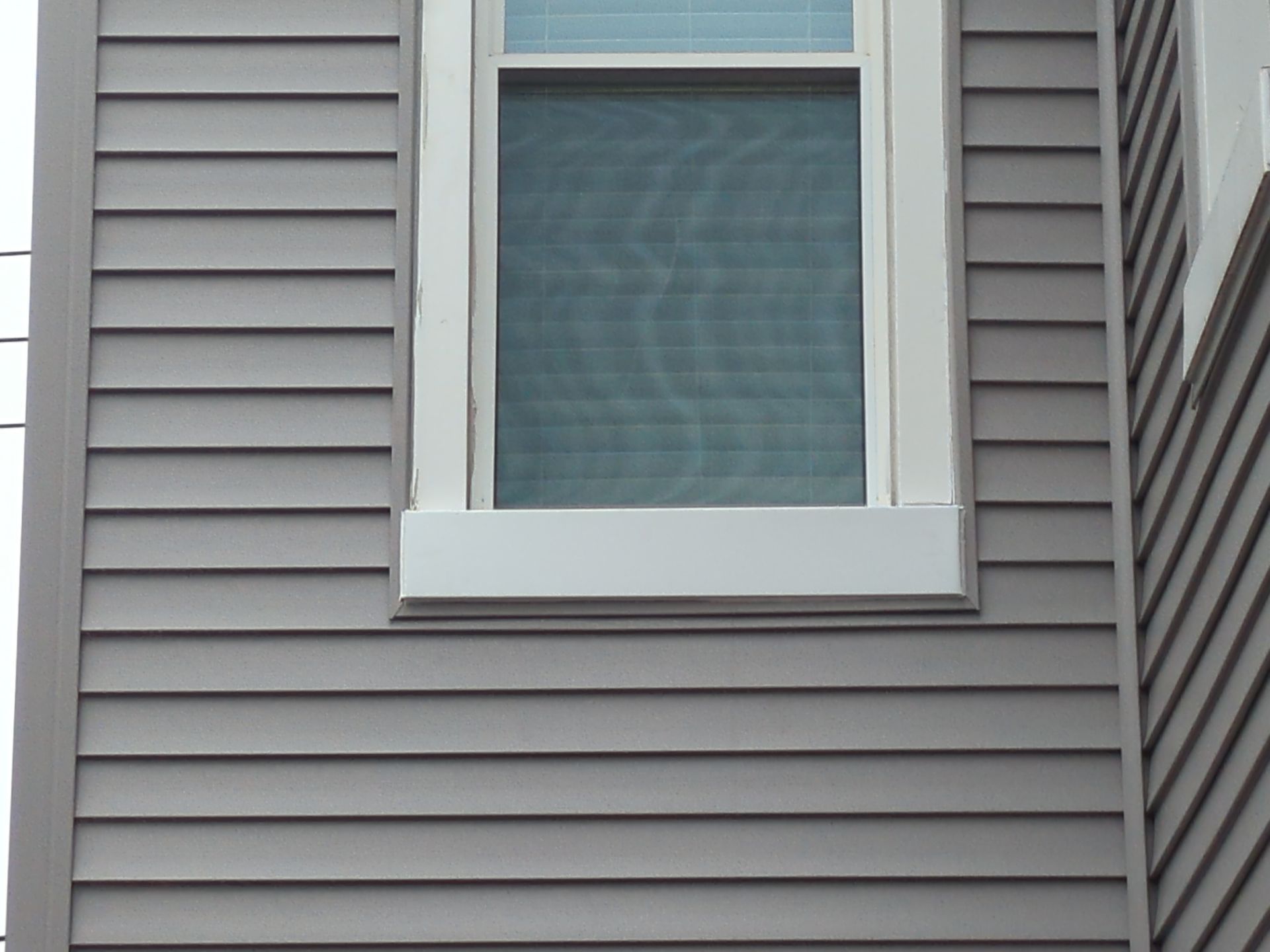 Gray horizontal siding with a white-framed window; exterior view.