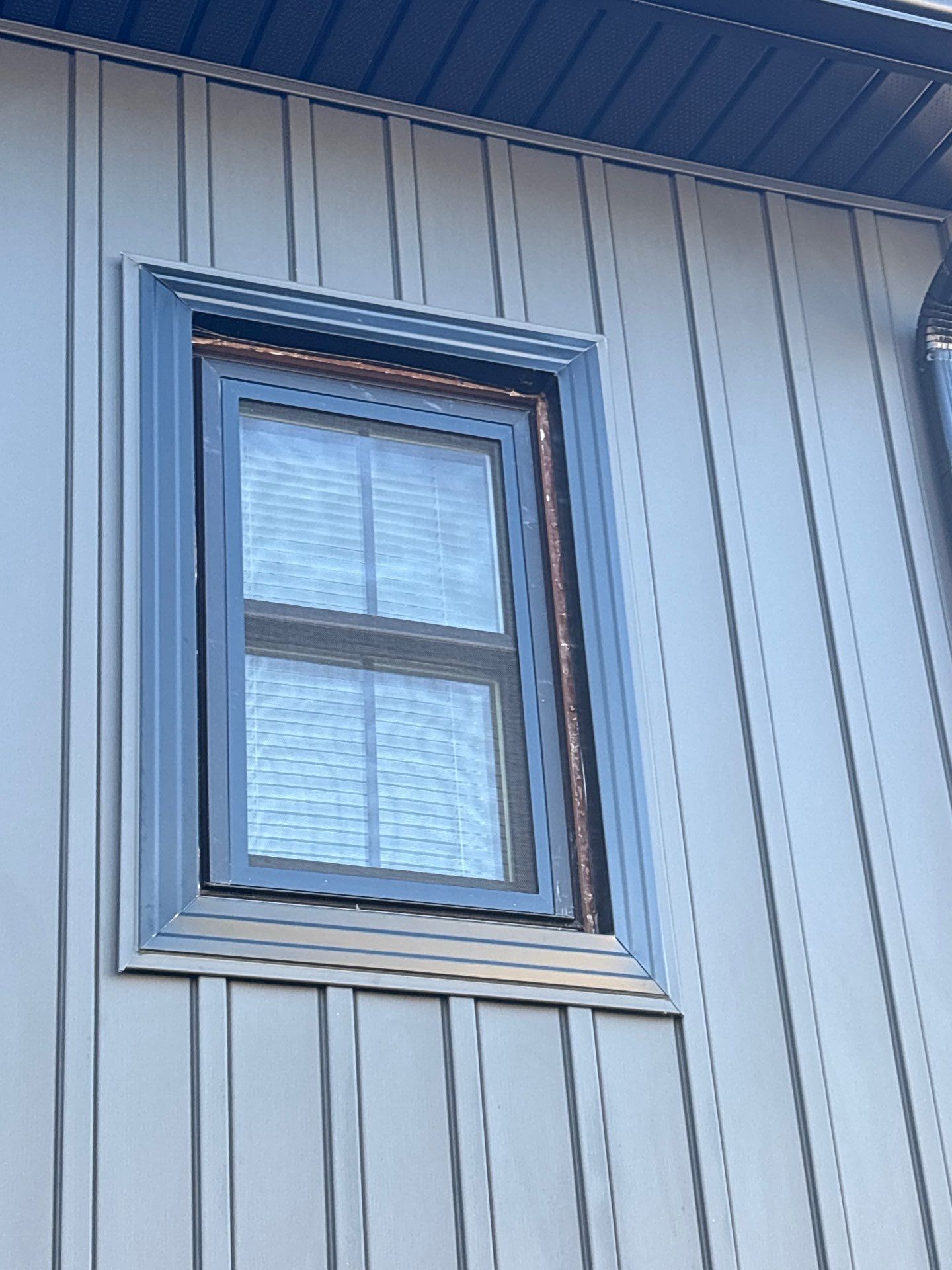 Blue-trimmed window on a gray-paneled exterior wall with blinds drawn