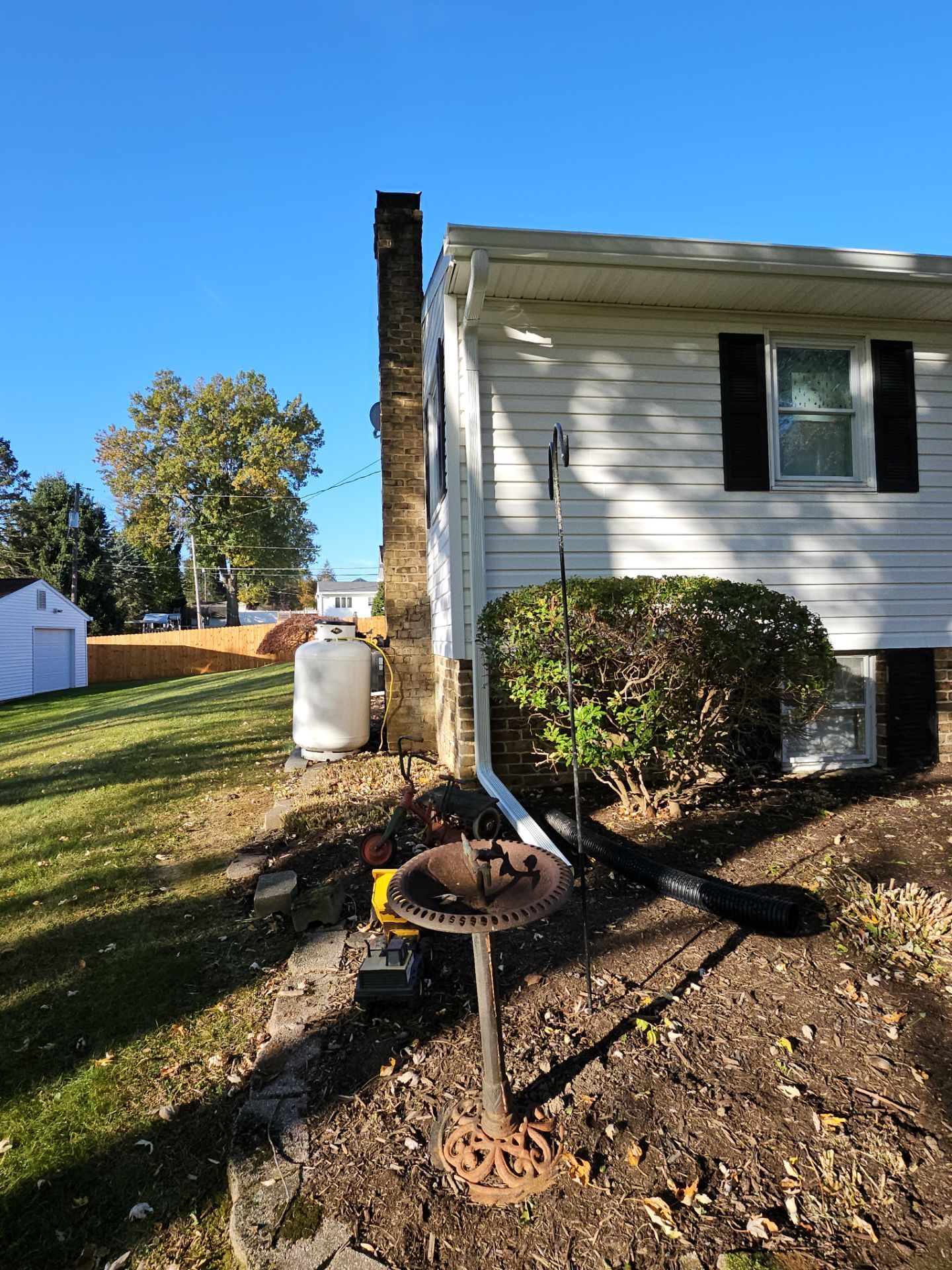 House side yard with a chimney, propane tank, and garden bed under a clear blue sky