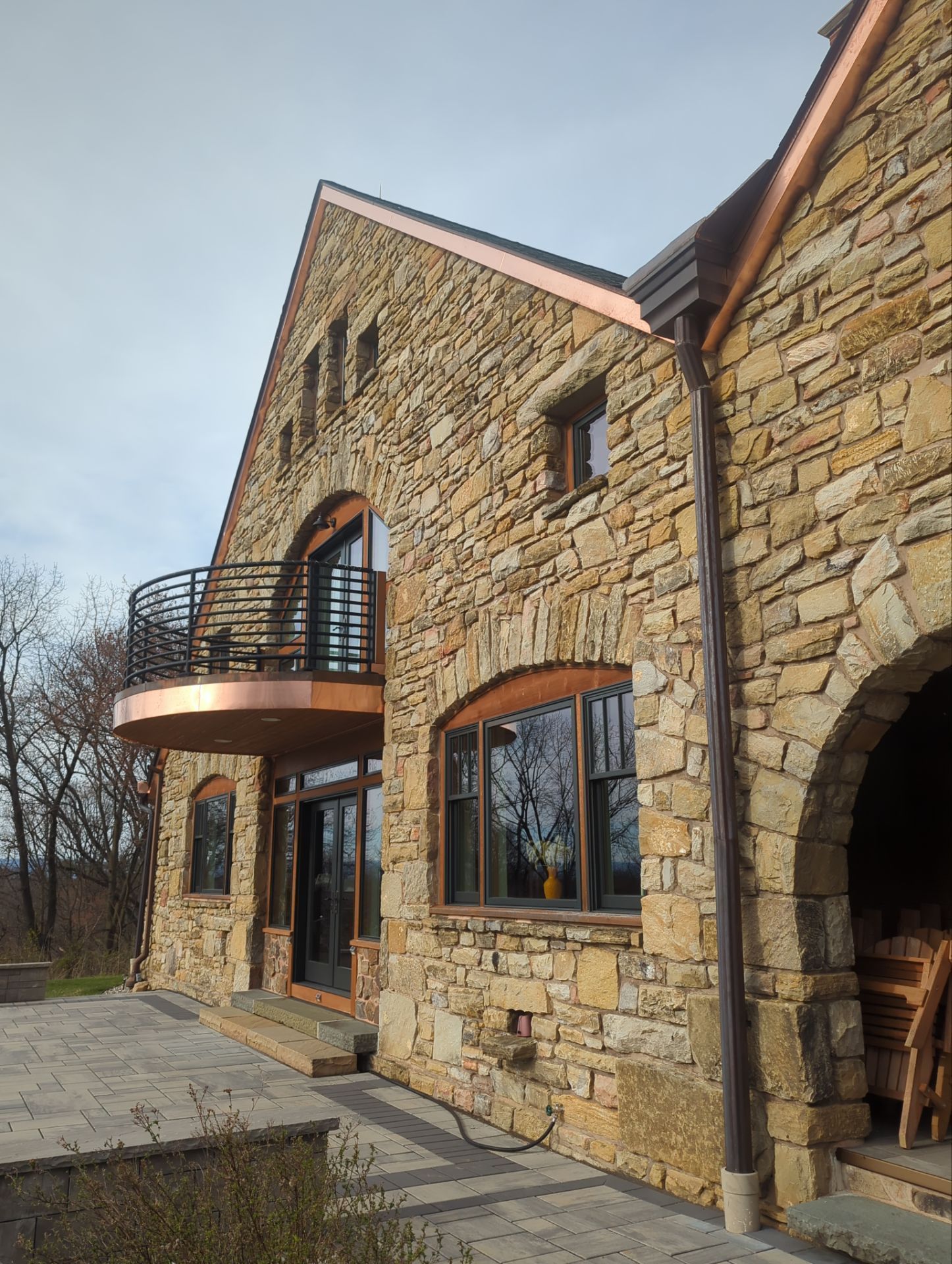 Stone house with copper accents and a balcony, under a cloudy sky.