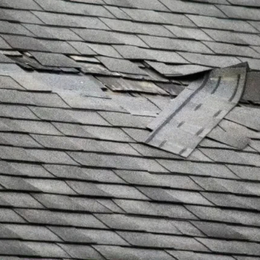 Damaged asphalt shingle roof with missing and torn shingles.
