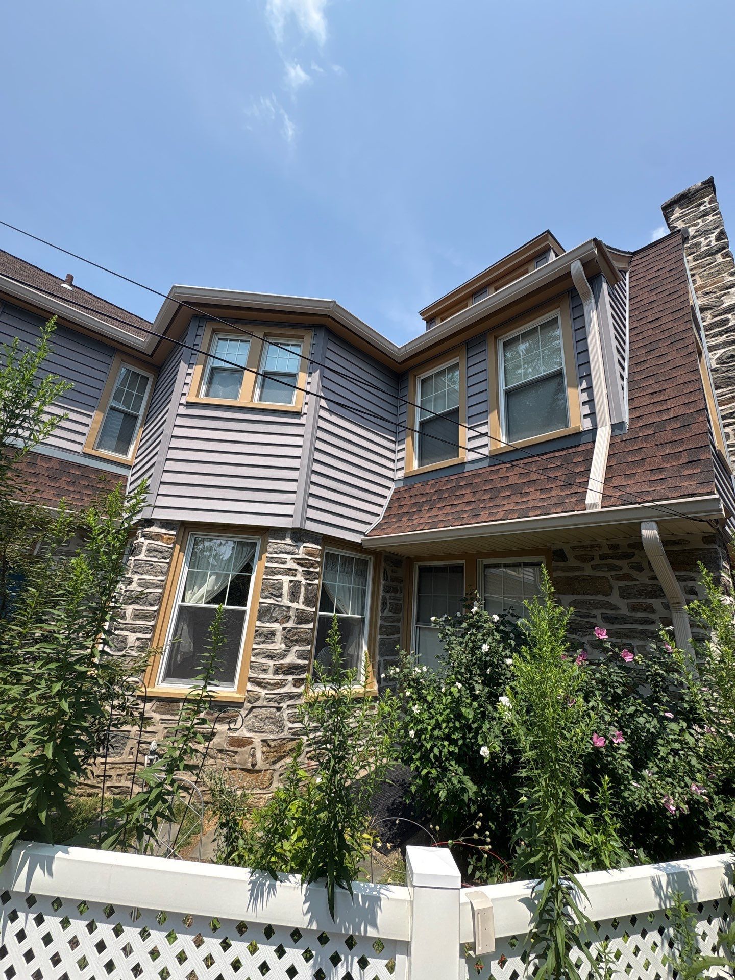 Stone and gray-sided house with a brown roof and white trim under a blue sky.