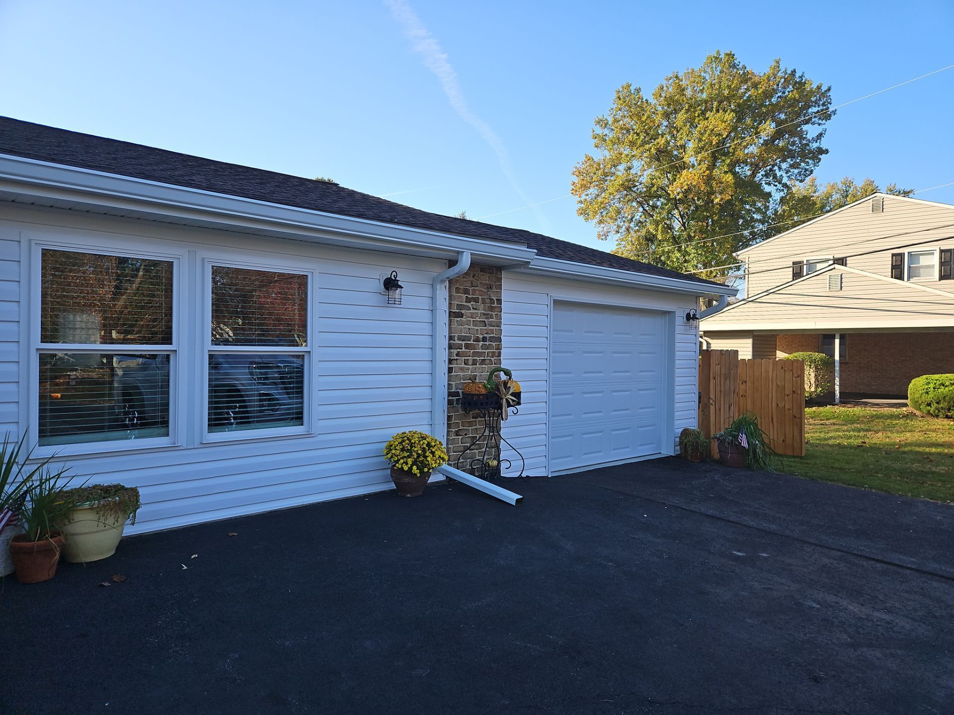 White house exterior with garage, black driveway, and a tree in the yard under a blue sky